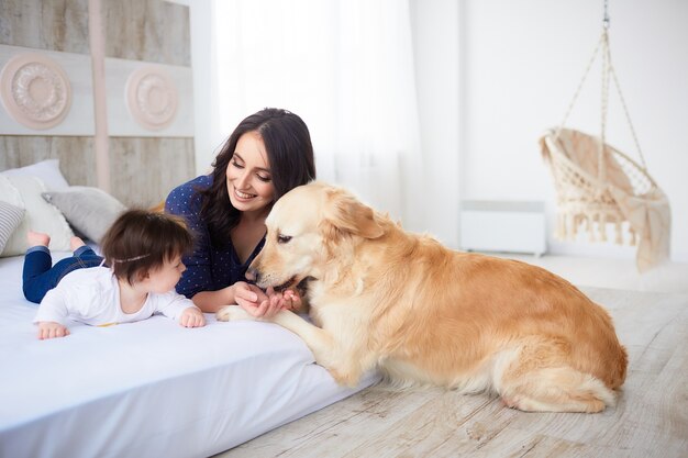 La madre con su hija se acuesta en la cama y el perro los mira