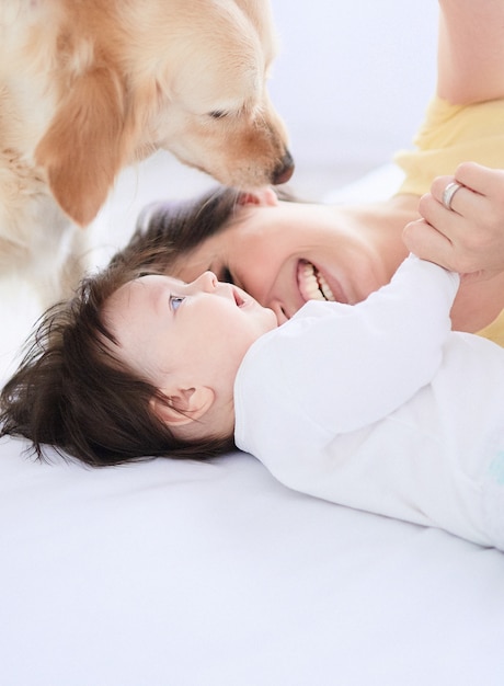 La madre con su hija se acuesta en la cama y el perro los mira