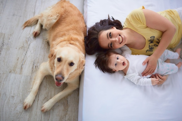 La madre con su hija se acuesta en la cama y el perro sentado cerca de la cama