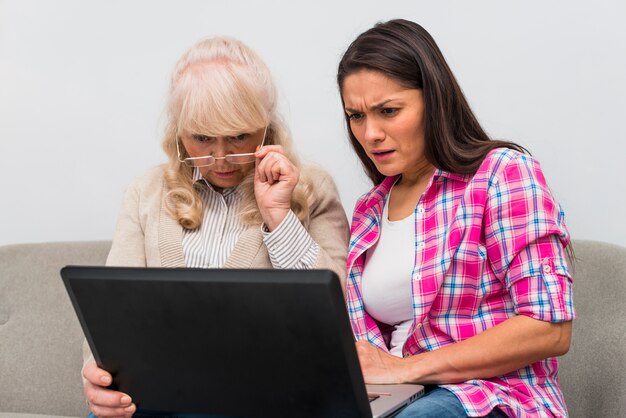 Madre y su hija adulta mirando portátil con curiosidad