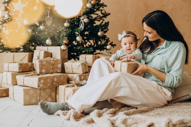 Madre con su hija con cajas de regalo por el árbol de Navidad