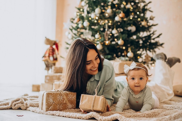 Madre con su hija con cajas de regalo por el árbol de Navidad
