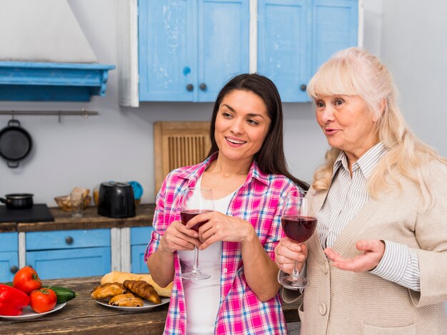 Madre y su hija joven de pie en la cocina con copas de vino en las manos