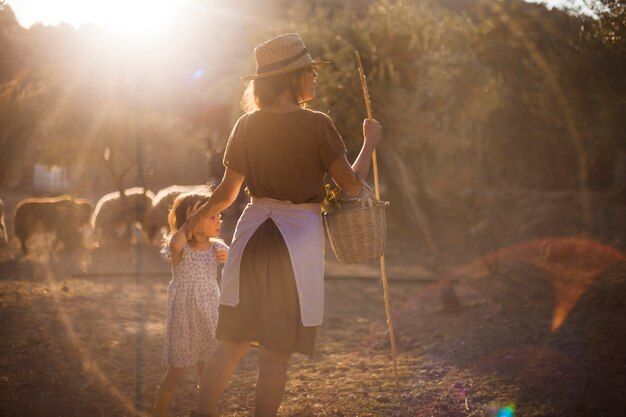 Madre con su hija sosteniendo canasta y palo en la granja