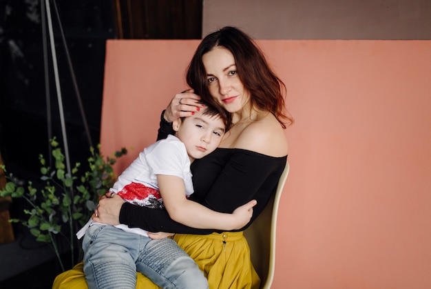 Madre y su hijo están posando en el estudio y vistiendo ropa informal.