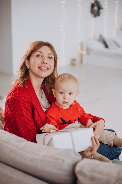 Madre con su hijo sentado en el sofá y desembalaje de regalos de Navidad