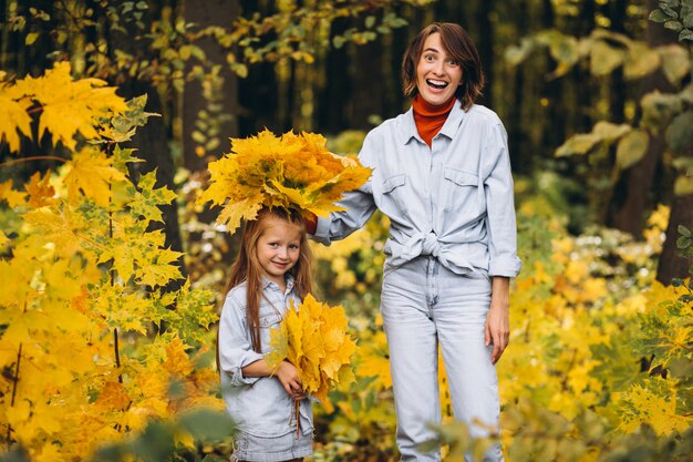 Madre con su pequeña hija en un bosque lleno de hojas doradas