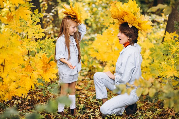 Madre con su pequeña hija en un bosque lleno de hojas doradas