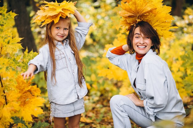 Madre con su pequeña hija en un bosque lleno de hojas doradas