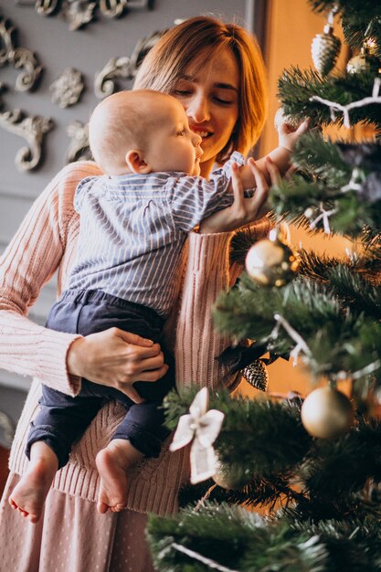 Madre con su pequeño hijo decorando el árbol de Navidad con juguetes