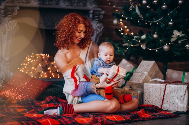 Madre con su pequeño hijo junto al árbol de navidad con regalos.