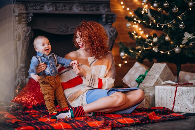 Madre con su pequeño hijo junto al árbol de navidad con regalos.