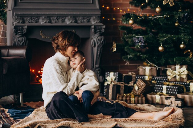 Madre con su pequeño hijo sentado junto al árbol de Navidad