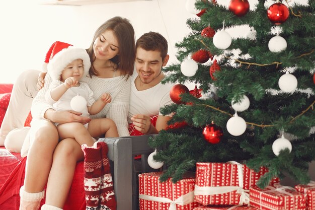 Madre con un suéter blanco. Familia con regalos de Navidad. Niño con padres en adornos navideños.