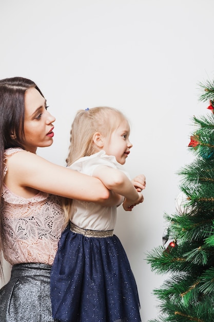 Madre sujetando hija enfrente de árbol de navidad