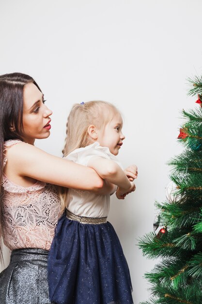 Madre sujetando hija enfrente de árbol de navidad