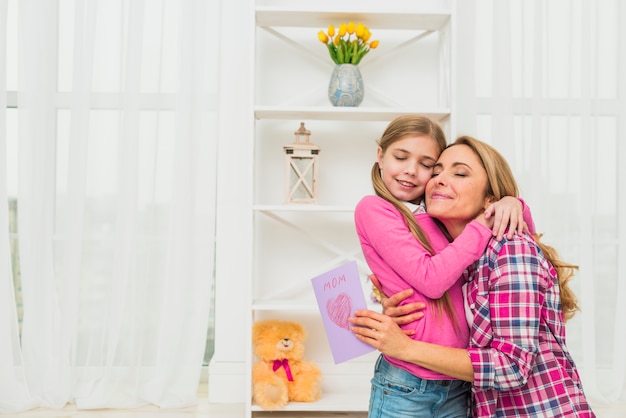 Madre con tarjeta de felicitación abrazando a hija