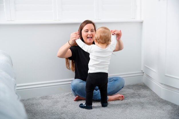 Madre de tiro completo ayudando a un niño a ponerse de pie