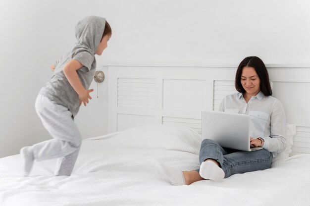 Foto gratuita madre de tiro completo con laptop y niño en la cama