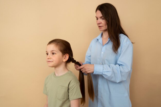 Madre de tiro medio trenzando el cabello de una niña.
