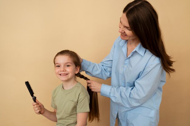 Madre de tiro medio trenzando el cabello de una niña.