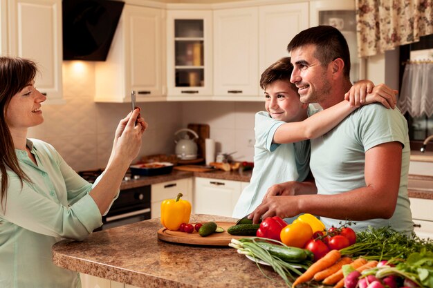 Madre tomando una foto de papá e hijo en la cocina