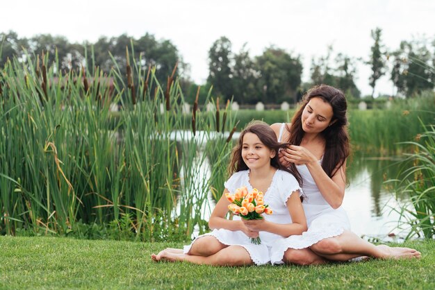 Madre trenzando el cabello de la hija junto al lago.