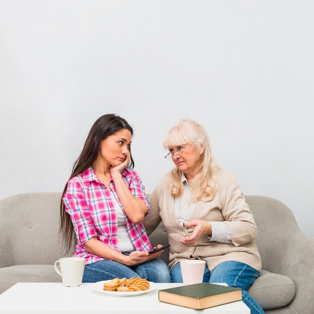 Madre triste e hija que se miran con el desayuno en la tabla blanca