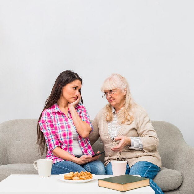 Madre triste e hija que se miran con el desayuno en la tabla blanca