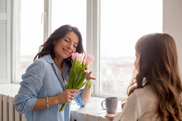 Madre con tulipanes e hija de pie en la ventana