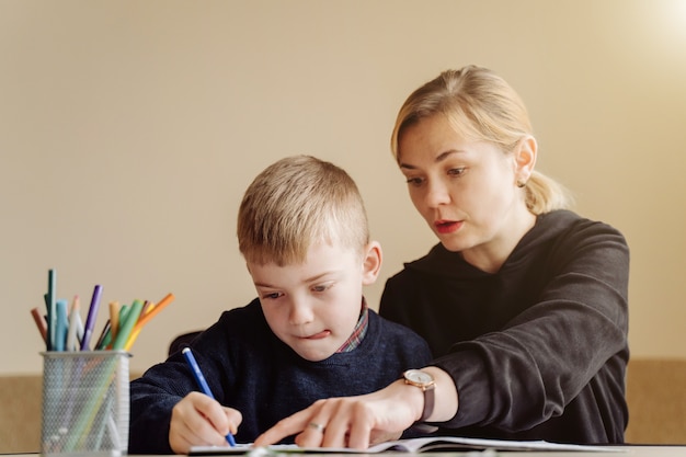Madre usando una computadora portátil y una tableta enseñando con su hijo en línea en su casa en su habitación