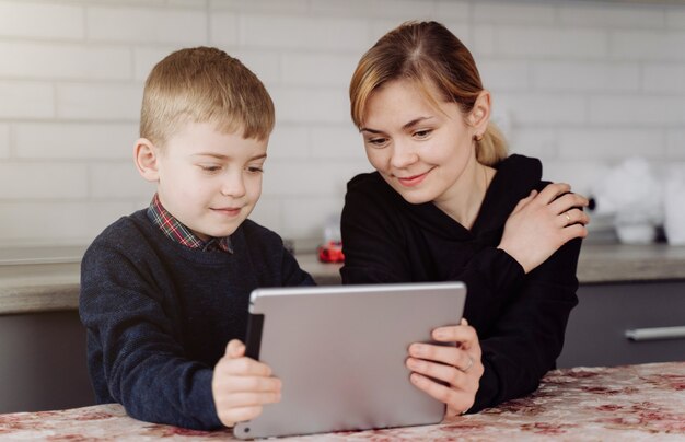 Madre usando una computadora portátil y una tableta enseñando con su hijo en línea en su casa en su habitación