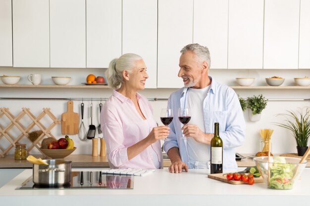 Madura feliz pareja amorosa de pie en la cocina bebiendo vino