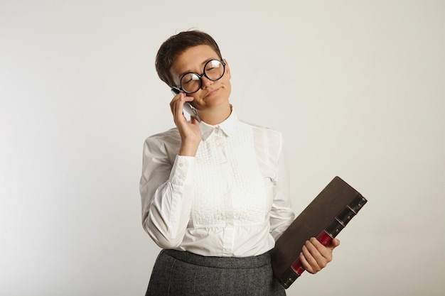 Maestra aburrida con un libro grande cierra los ojos con exasperación blanca hablando por teléfono