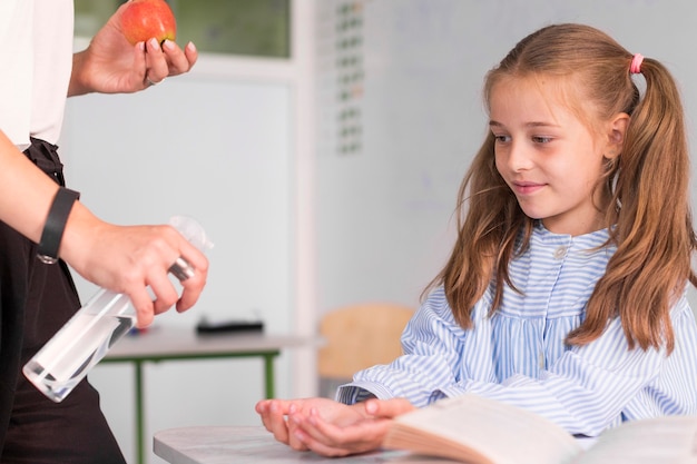 Maestra ayudando a niña a desinfectar sus manos