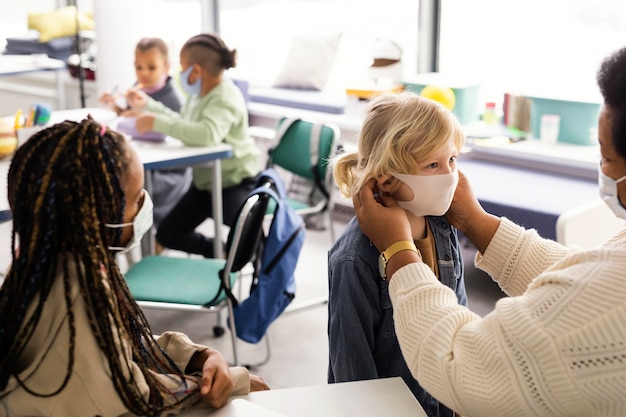 Maestra ayudando a los niños con su máscara médica