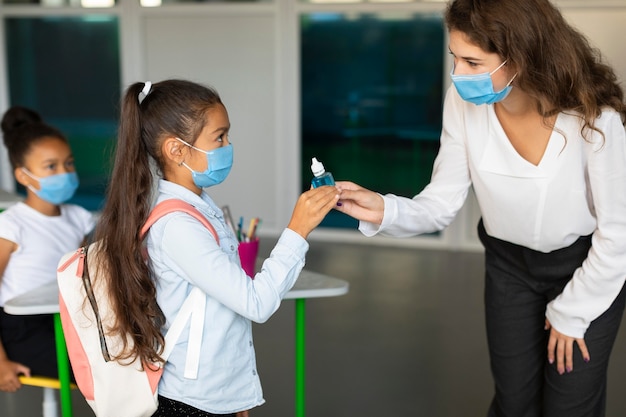 Maestra desinfectando las manos de su alumno en clase