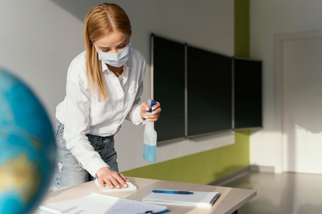 Maestra desinfectar su escritorio en el aula