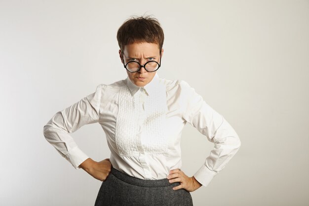 Maestra enojada en gafas negras redondas y traje conservador con el ceño fruncido aislado en blanco