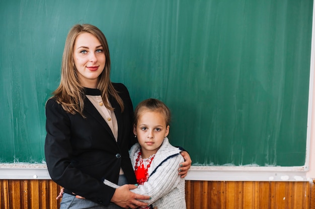 Foto gratuita maestra con estudiante chica de pie y abrazos