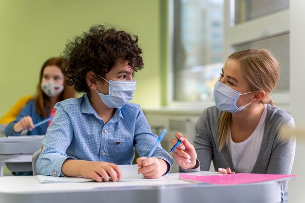 Maestra con máscara médica ayudando a los estudiantes en clase