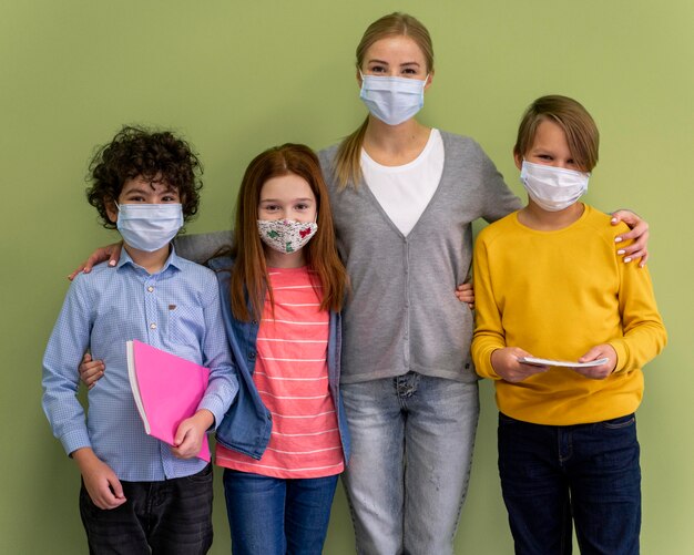 Maestra con máscara médica posando con niños en la escuela