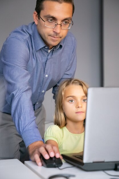 Maestra de mediana edad revisando la tarea y de pie detrás de la niña