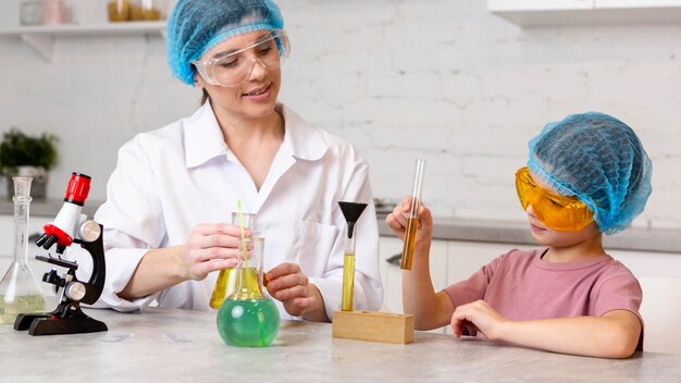 Maestra y niña con redecillas para el cabello haciendo experimentos científicos con microscopio