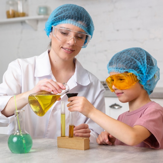 Maestra y niña con redecillas para el cabello haciendo experimentos científicos con tubos de ensayo