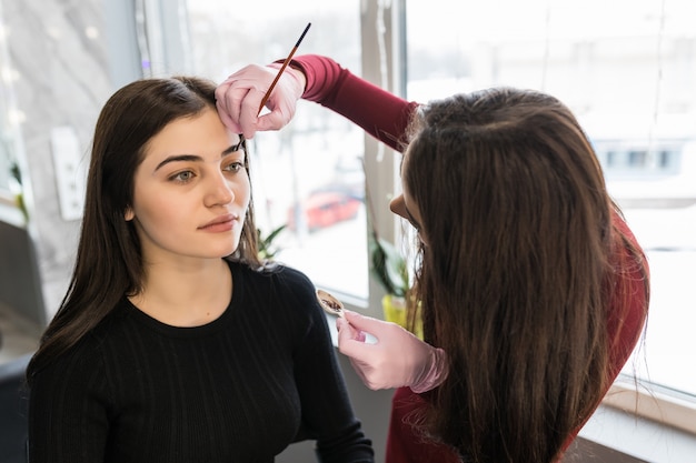 Maestra pone pintura de cejas con pincel durante el procedimiento de maquillaje