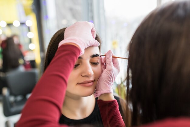 Maestra pone pintura de cejas en salón de belleza durante el procedimiento de maquillaje