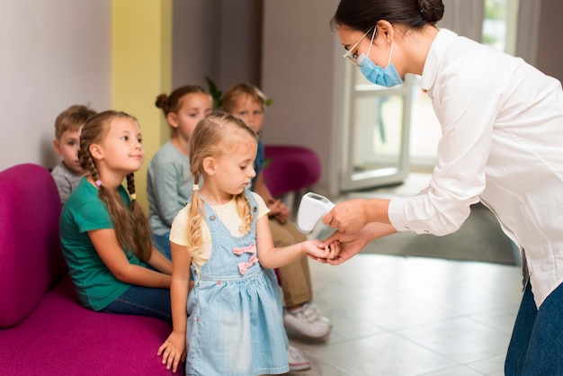 Maestra revisando la temperatura de sus alumnos en tiempo de pandemia