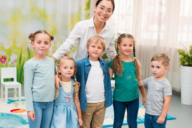 Maestra sonriente sosteniendo a sus alumnos en el jardín de la infancia