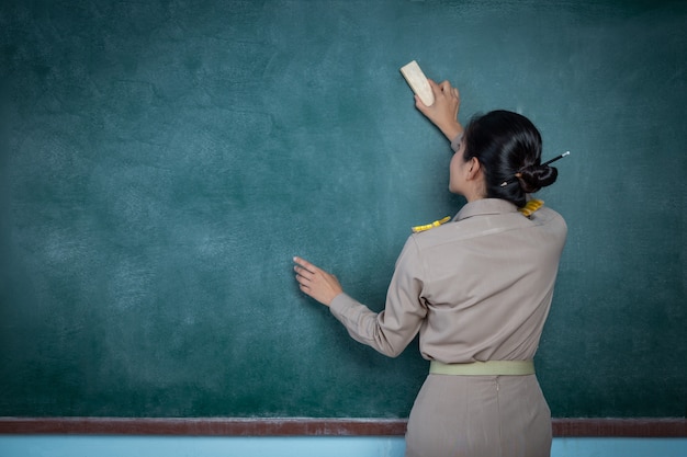 Foto gratuita maestra tailandesa en traje oficial borrando pizarra